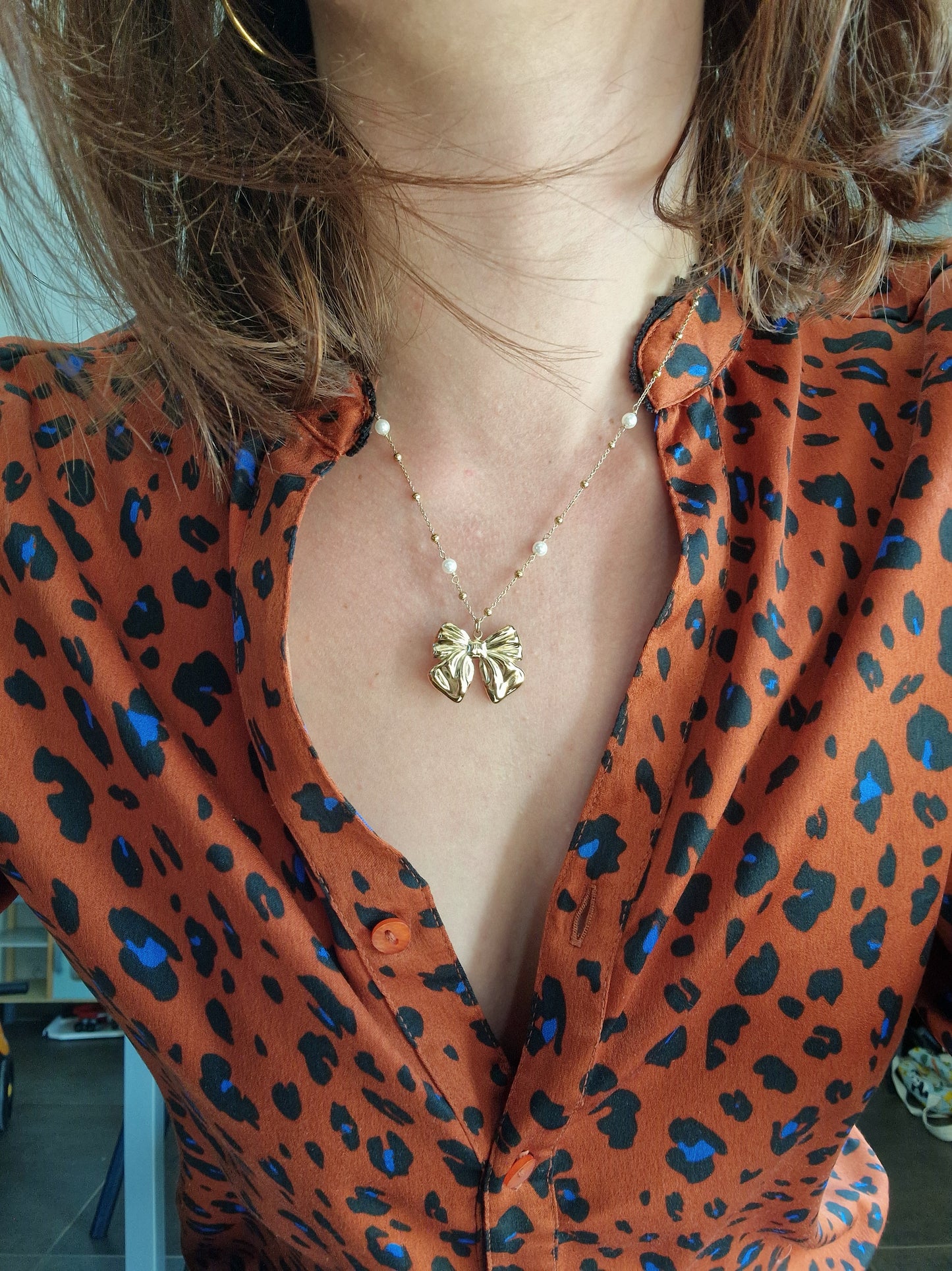 Collier nœud en acier inoxydable couleur or porté sur une robe imprimée, fin et délicat avec imitation perles élégantes.